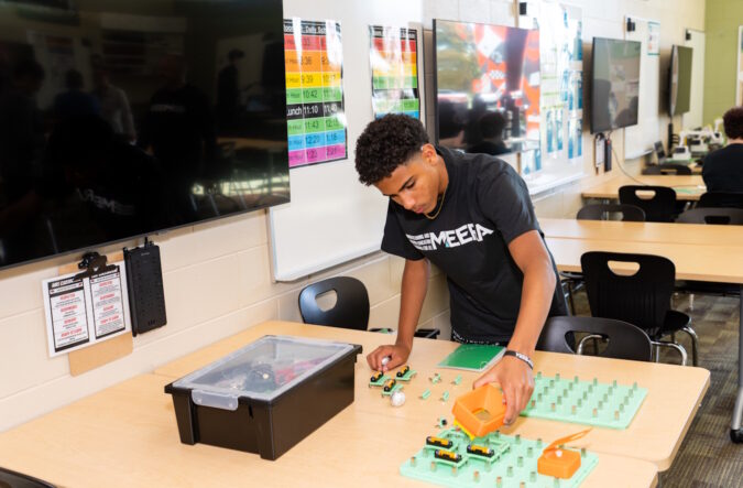 A young man leaning over a table with various parts laid out on it.