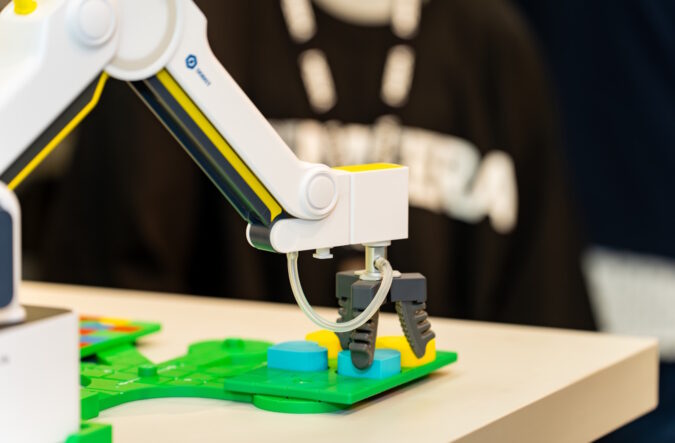 A robotic arm picking up pieces of plastic laid on a table.